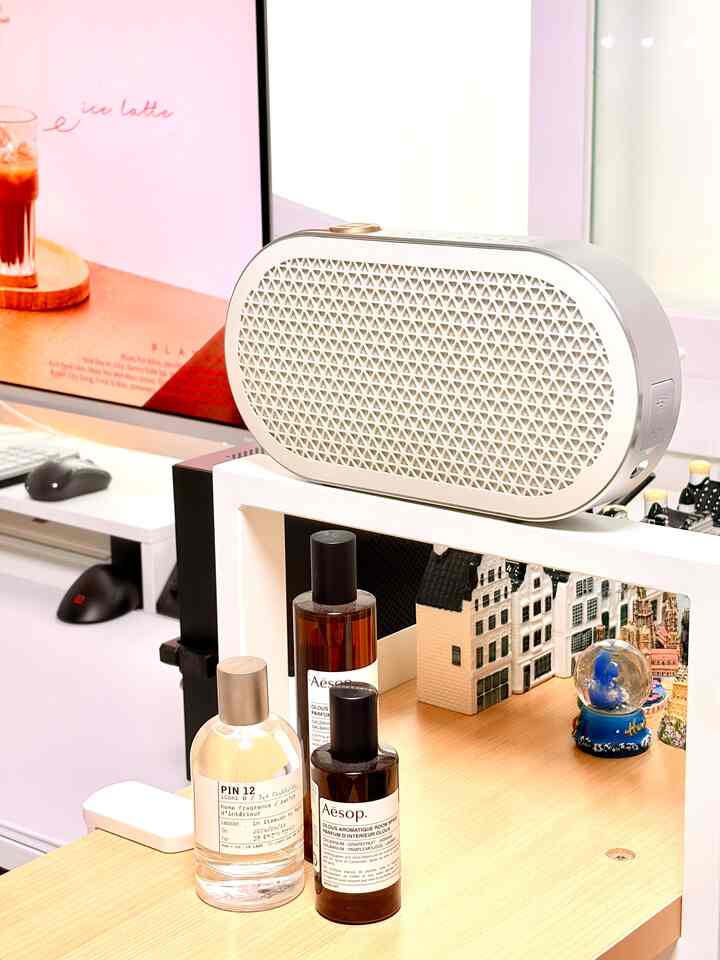ホワイトと穏やかなブラウンの色調の小さなホームオフィス空間、楕円形のスピーカーとイソップのルームスプレーが置かれた整ったデスクのインテリア