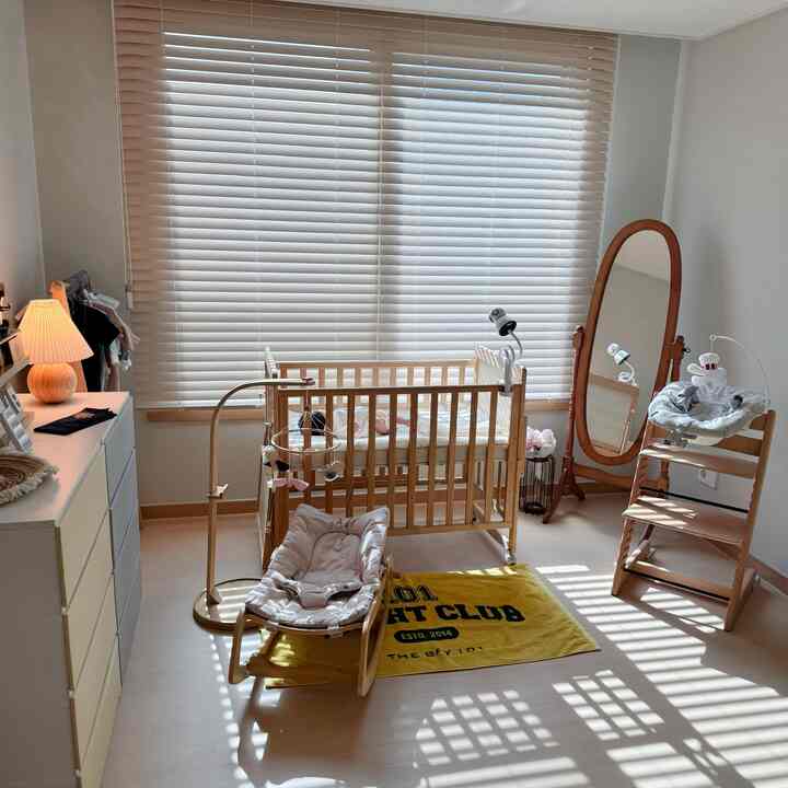 明るいホワイトと木目調の調和した赤ちゃん部屋、木製ベビーベッドとベビーチェア、姿見鏡が配置された自然な空間