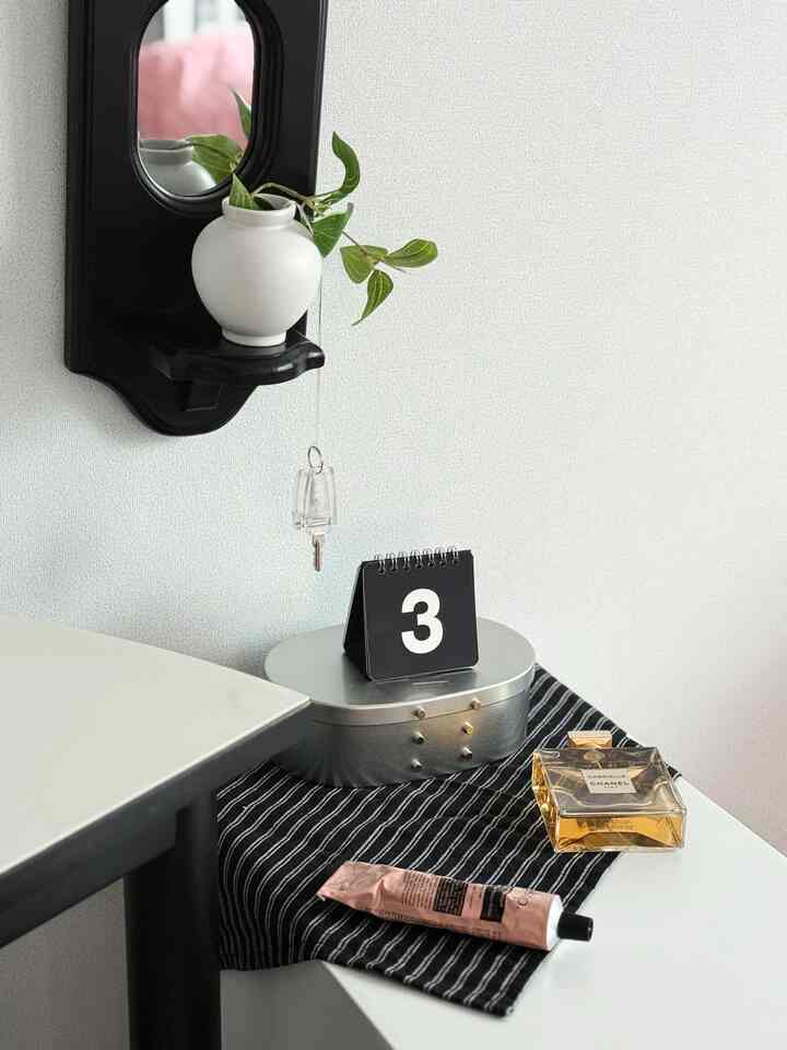 白い壁の背景にミニマルな玄関空間、黒い額縁の鏡、金属製キャビネットと装飾品が調和した雰囲気のあるインテリア