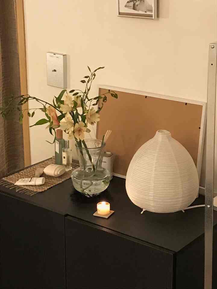ナチュラルカラーの壁が背景の空間、黒い収納棚の上に花瓶とキャンドル、和紙風のランプが配置された居心地の良いインテリア