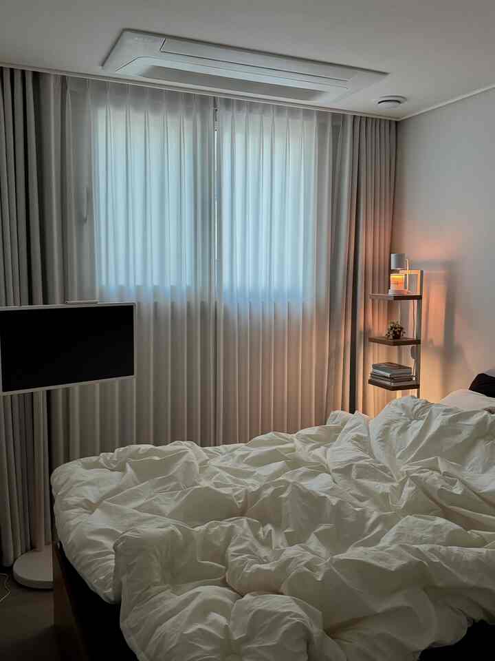 White and beige toned bedroom featuring a bed, blackout curtains, and a floor lamp, creating a cozy atmosphere