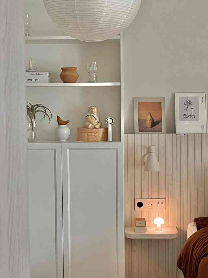 白を基調とした壁と本棚が配置された寝室、ナチュラルモダンな小物と暖かな照明が調和した雰囲気のあるインテリア