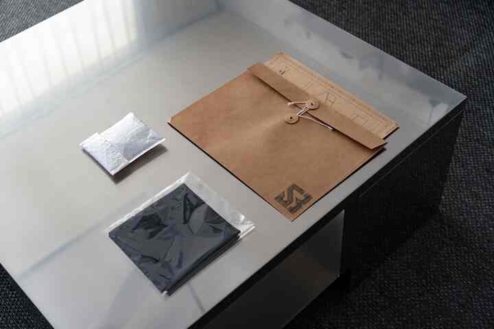 シルバーの金属テーブルに茶色の書類フォルダーと小物が置かれた、シンプルモダンな印象的な空間