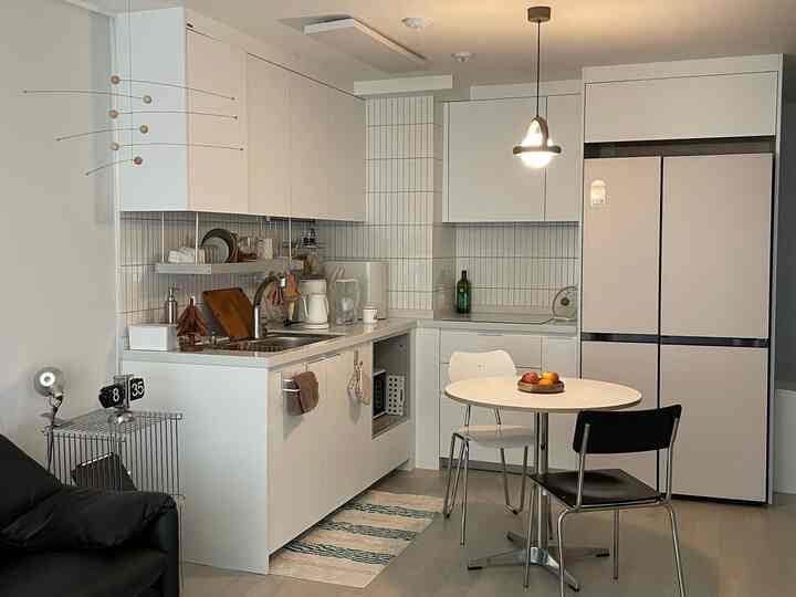 明るいホワイトトーンのキッチン、ラウンドダイニングテーブルとベージュの冷蔵庫が配置されたコンパクトで整った空間