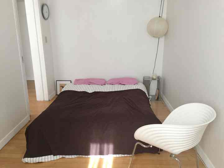 白い壁とナチュラルウッドの床が調和したモダンな寝室、ブラウンの掛け布団とピンクの枕がアクセントのすっきりとした空間