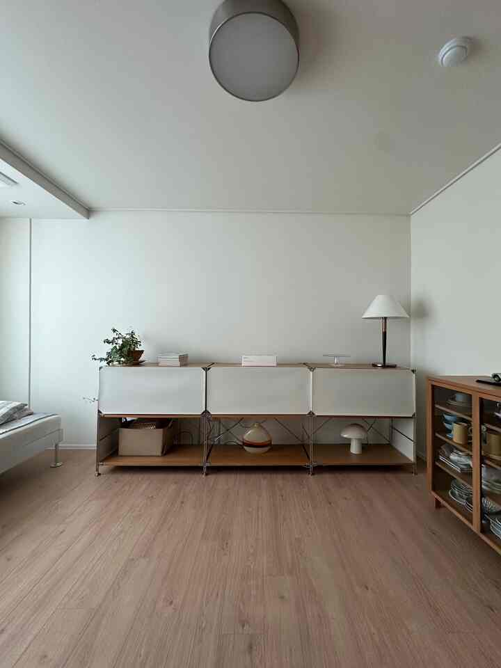 ナチュラルな木目調の床と白い壁のリビング、中央にキャビネットが配置されシンプルモダンな雰囲気のインテリア