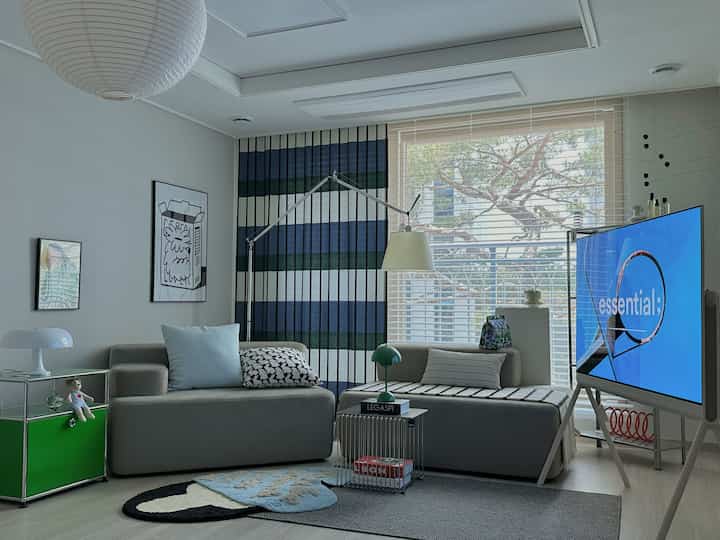 淡いカーキ色のモジュラーソファと青のストライプカーテンが調和するモダンなリビング空間