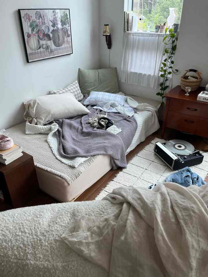 白と木目調が調和したナチュラルで居心地の良いワンルームの寝室、枕とナイトテーブルが配置された印象的な空間