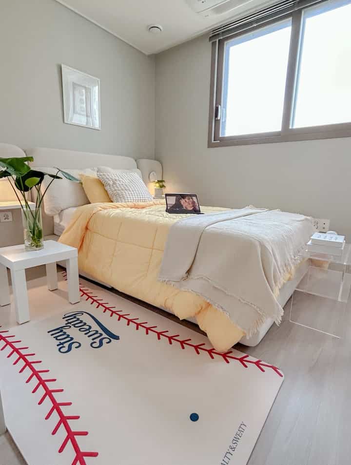 白と黄色のトーンの寝室、大きな窓と黄色のベッドカバーが配された印象的な空間