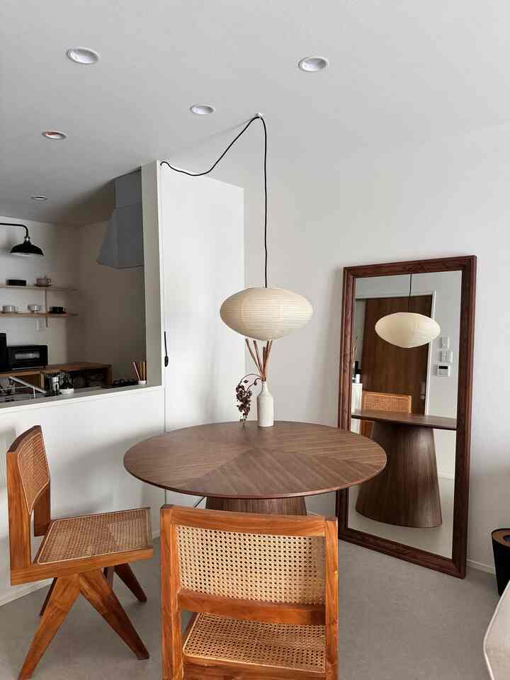 ナチュラルカラーと白い壁のダイニング、ラタンチェアと丸い木製ダイニングテーブルが配置された雰囲気のあるインテリア