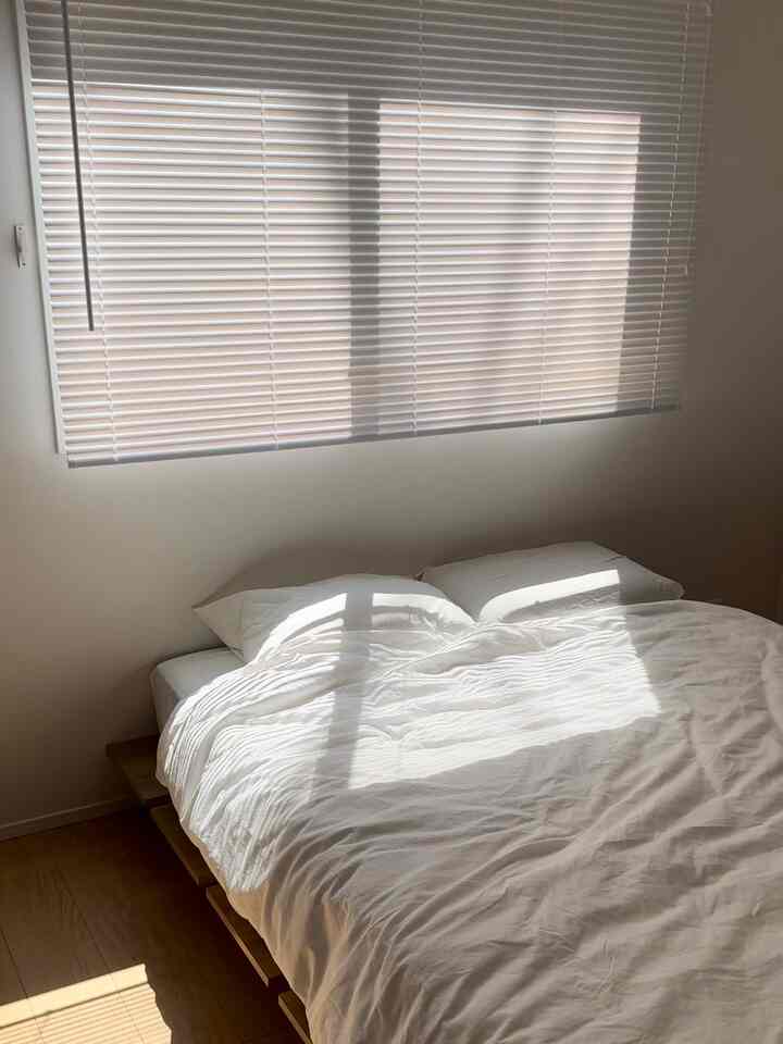 白と木目調が調和する寝室、ブラインドの窓とダブルベッドが配置された自然で落ち着いたインテリア