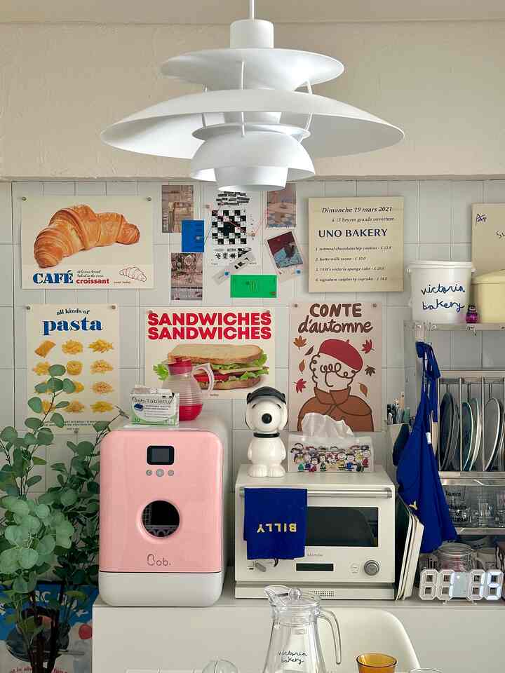 白いタイル壁とピンクの食洗機、ルイスポールセンのペンダントライトがあるコンパクトで居心地の良いキッチン・ダイニングスペース