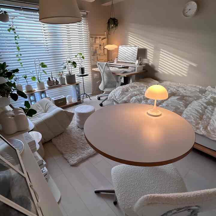 アイボリーとホワイトの色調の一人暮らし向けリビング兼ダイニング、丸テーブルとデスク、ベッドが配置された落ち着いた雰囲気の空間