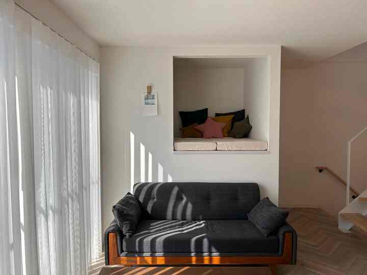 ナチュラルカラーのリビング、ダークグレーのソファと壁の奥にクッションが配置されたヌックのある雰囲気の良い空間