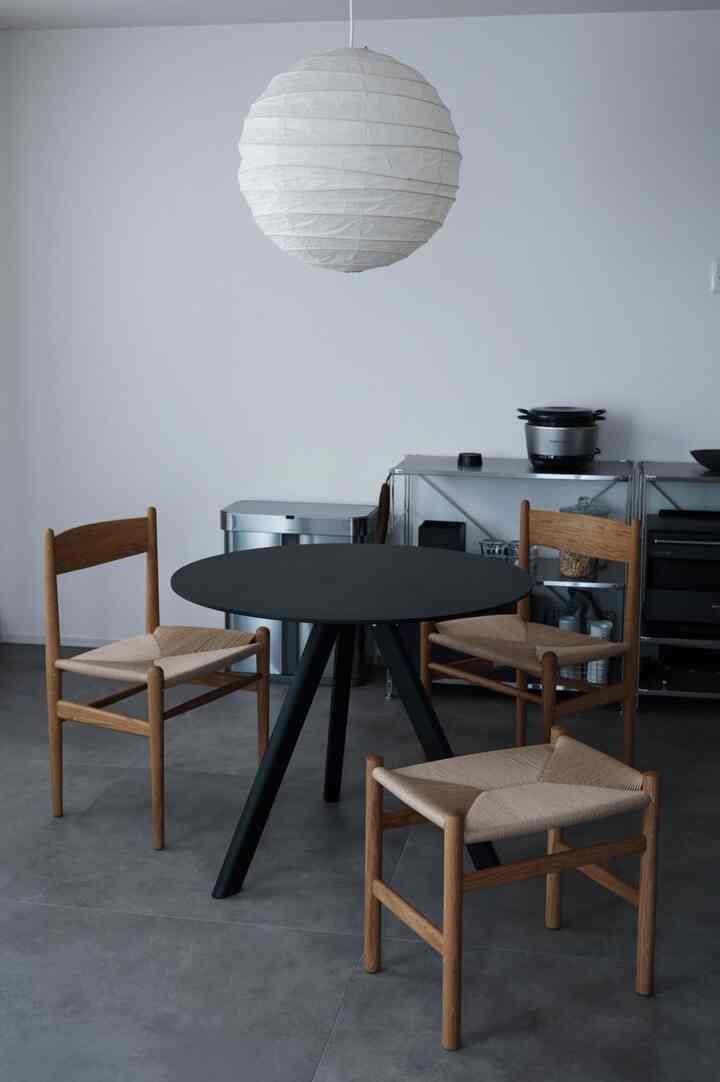 白い壁と黒い丸テーブルを配したナチュラルモダンなダイニング、木製の椅子とペンダントライトが配置されたシンプルで落ち着いた空間