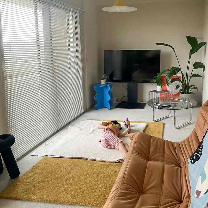 ベージュと黄色の落ち着いた色調のリビング、ブラウンのソファと大型テレビ、植物が配置された自然な雰囲気のインテリア