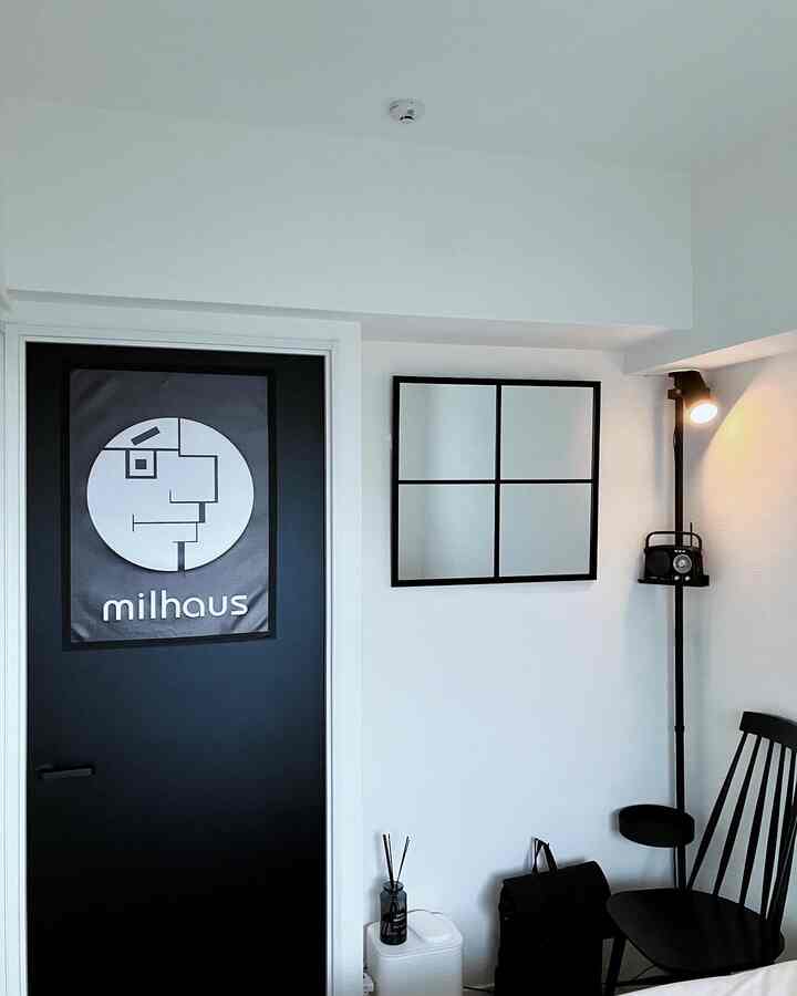 モノトーンの黒と白の玄関、黒いドアと中央の壁掛け鏡、フロアランプと椅子が配置されたシンプルなインテリア