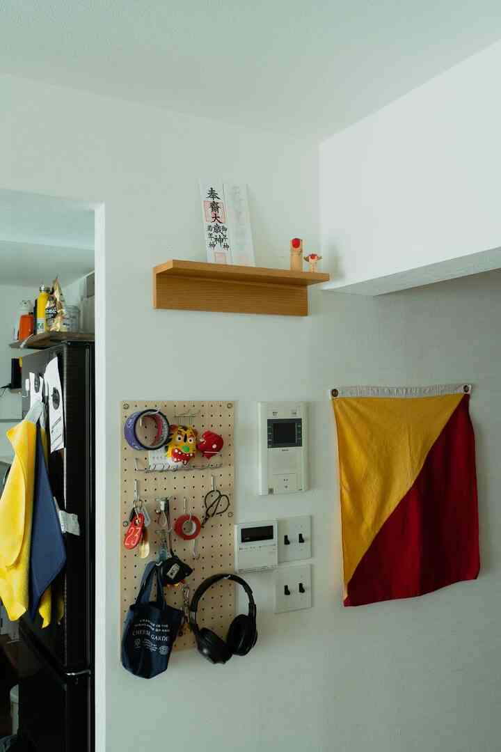 明るい白壁とナチュラルな木調の有孔ボードと棚が配置された玄関の収納アイデアのある空間