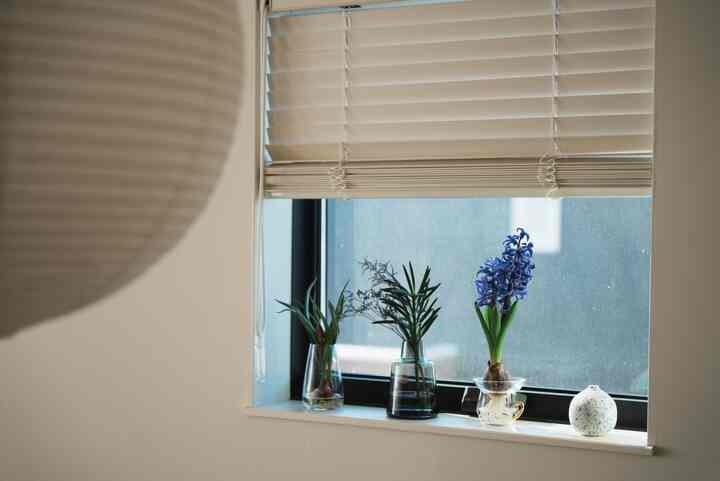 ベージュのブラインドがかかったダイニングの窓辺に、三つの花瓶が並び、自然な雰囲気のあるモダンな空間