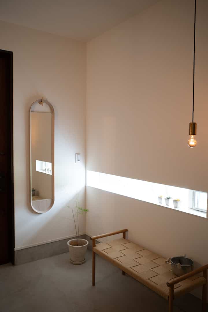 自然な木目調のベンチと長い楕円形の鏡が配置された明るくシンプルな玄関のインテリア