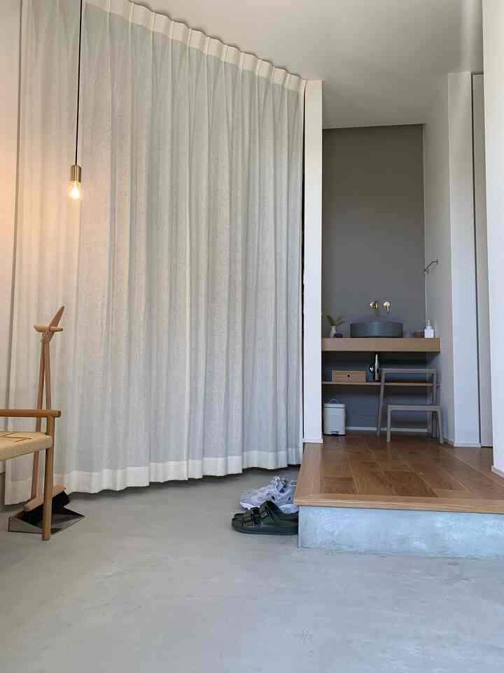 アイボリーのリネンカーテンと木目調の床が調和した、ナチュラルでシンプルな印象の玄関と洗面スペース