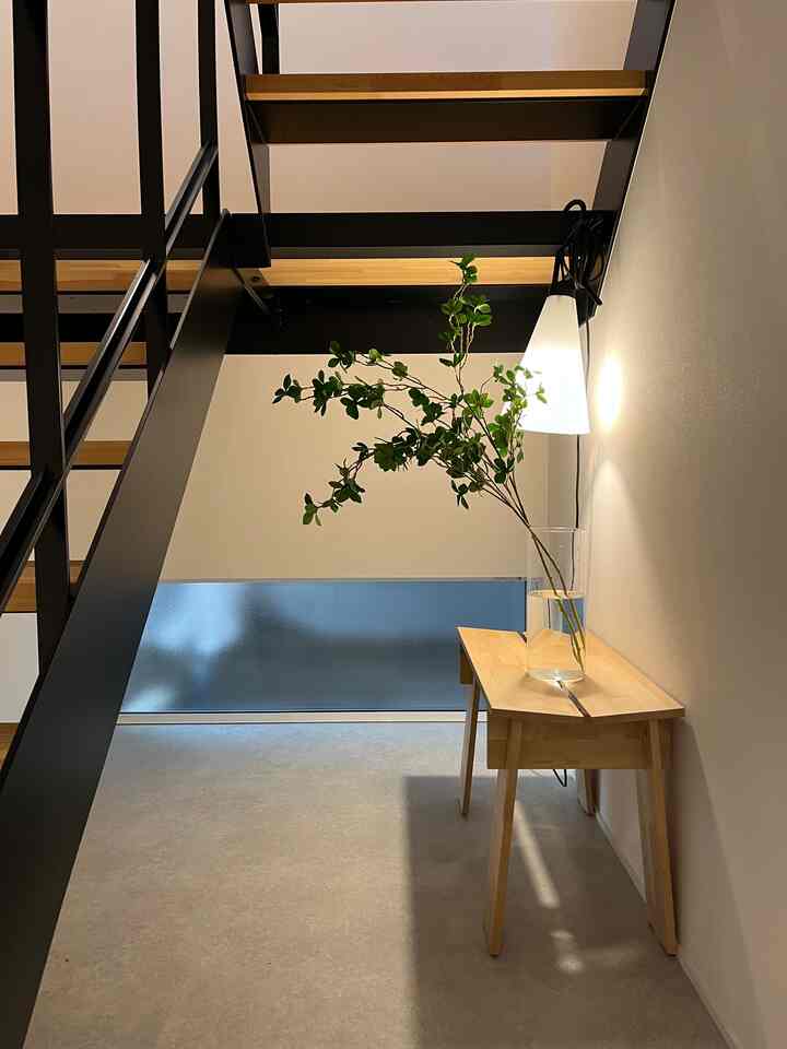 ナチュラルな色調の階段下空間、木製のテーブルと植物が置かれたミニマルで落ち着いた雰囲気のインテリア