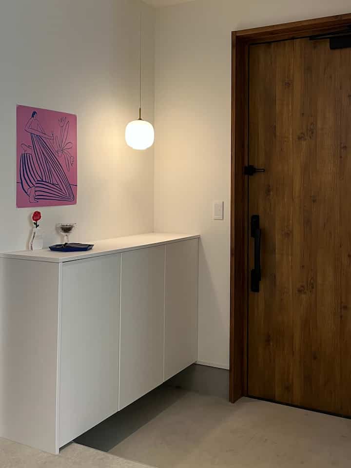 白と茶色のトーンの玄関、ルイスポールセンのラジオハウスペンダントライトが中央に掛かるシンプルな空間