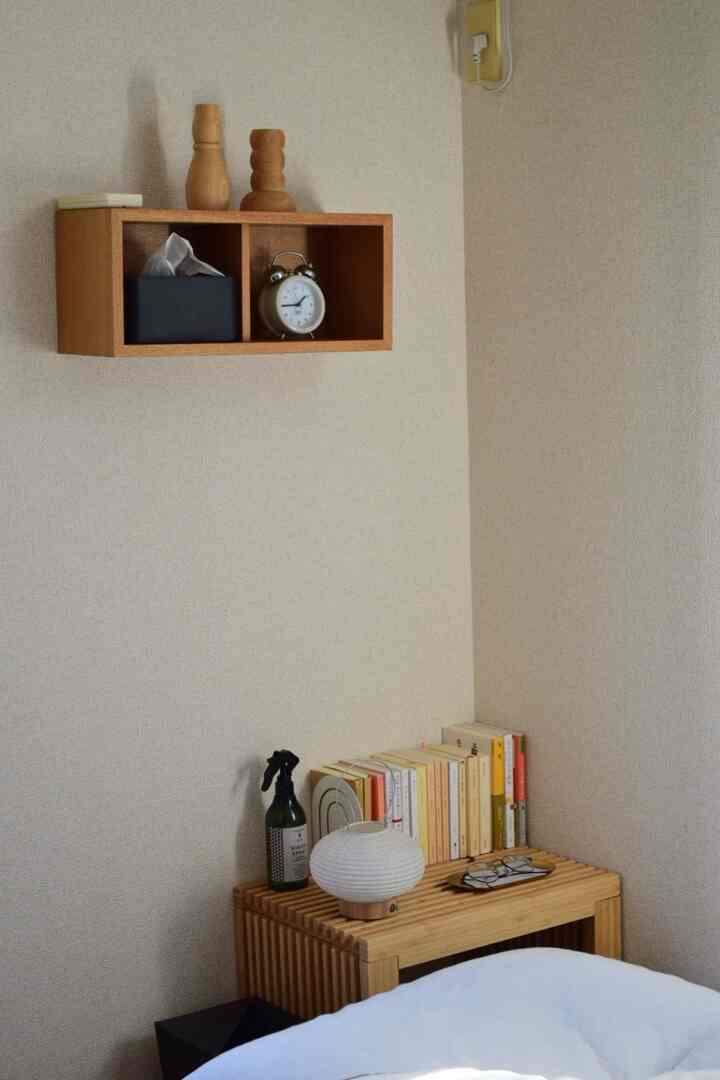 ナチュラルなベージュの壁と木製の棚、本やオブジェが並ぶ温かみのある寝室の一角