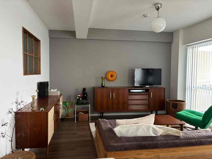 ダークウッド調とグレーの壁が調和したミッドセンチュリーモダンのリビング、ブラウンのソファとグリーンのアームチェアが配置された落ち着いた空間