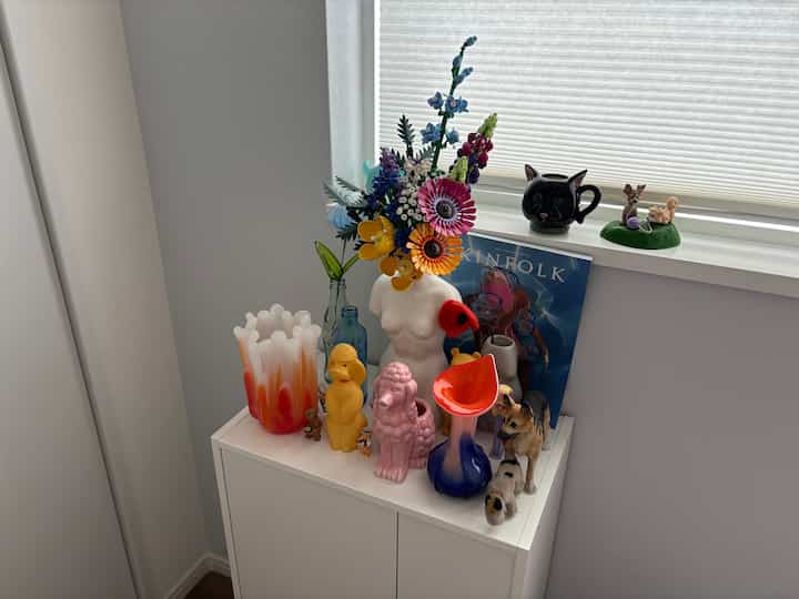 白を基調とした収納棚の上にカラフルなフェイクフラワーとペットのフィギュアが置かれた雰囲気のあるインテリア