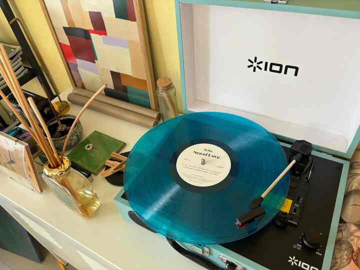 黄色い壁とスカイブルーのレコードプレイヤーがある印象的なインテリア空間、ポスターやディフューザー、テーブルランプが配置された雰囲気のある部屋