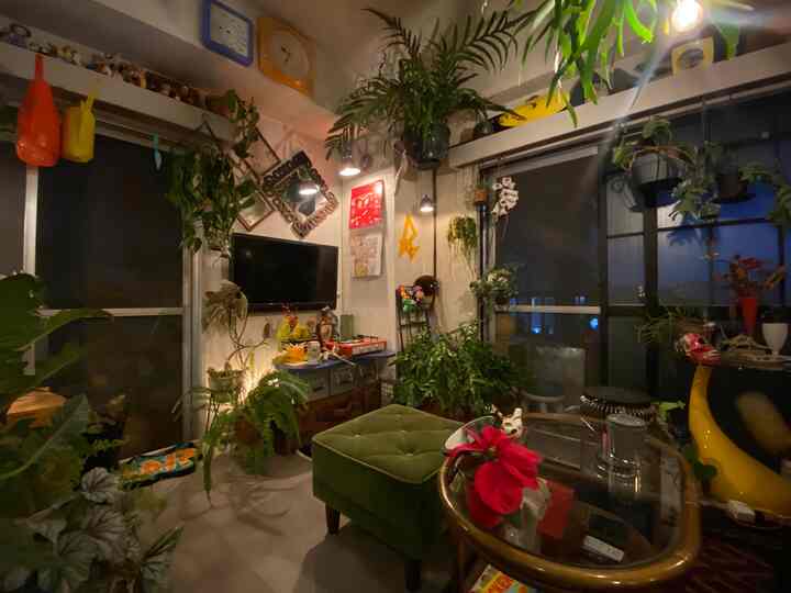 緑の植物が豊富なリビングスペース、グリーンのオットマンと壁照明が調和した自然な雰囲気のインテリア