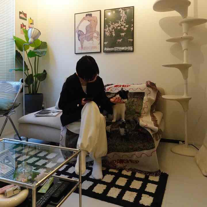 白と黒のモノトーンのリビング、ベージュのソファと透明なガラス製ローテーブル、猫とキャットタワーが配置されたシンプルな空間