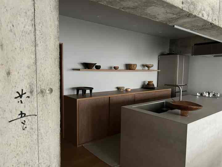 チャコールと木目調が調和したモダンなキッチン、壁の棚とサイドボードにオブジェが配置された印象的な空間