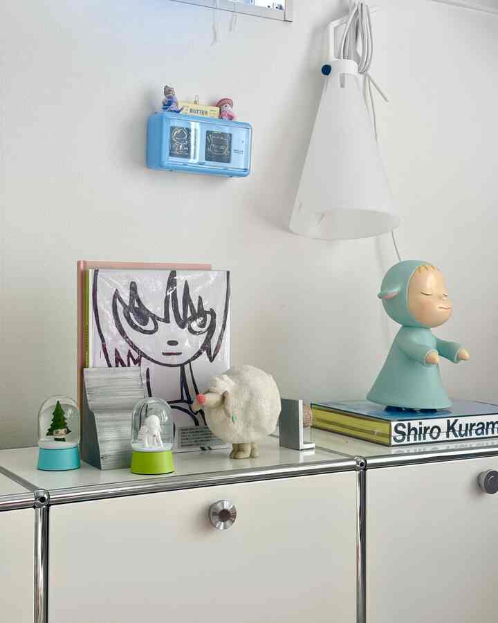 白とシルバーのトーンの壁とキャビネット、本やアート作品が配置された印象的なミニマル空間