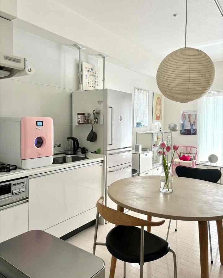 白とピンクの色調が広がるキッチンとダイニング、シンプルでミニマルな家具配置が印象的な空間
