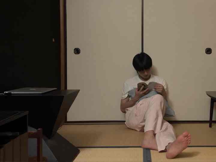 ベージュとブラックの色調のワンルーム、床に座って読書する人がいる自然でモダンな印象的な空間