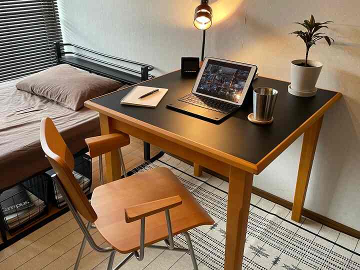 ベージュとブラウンの色調のワンルーム寝室、机の上にタブレットと植物が置かれた雰囲気のあるホームオフィス空間