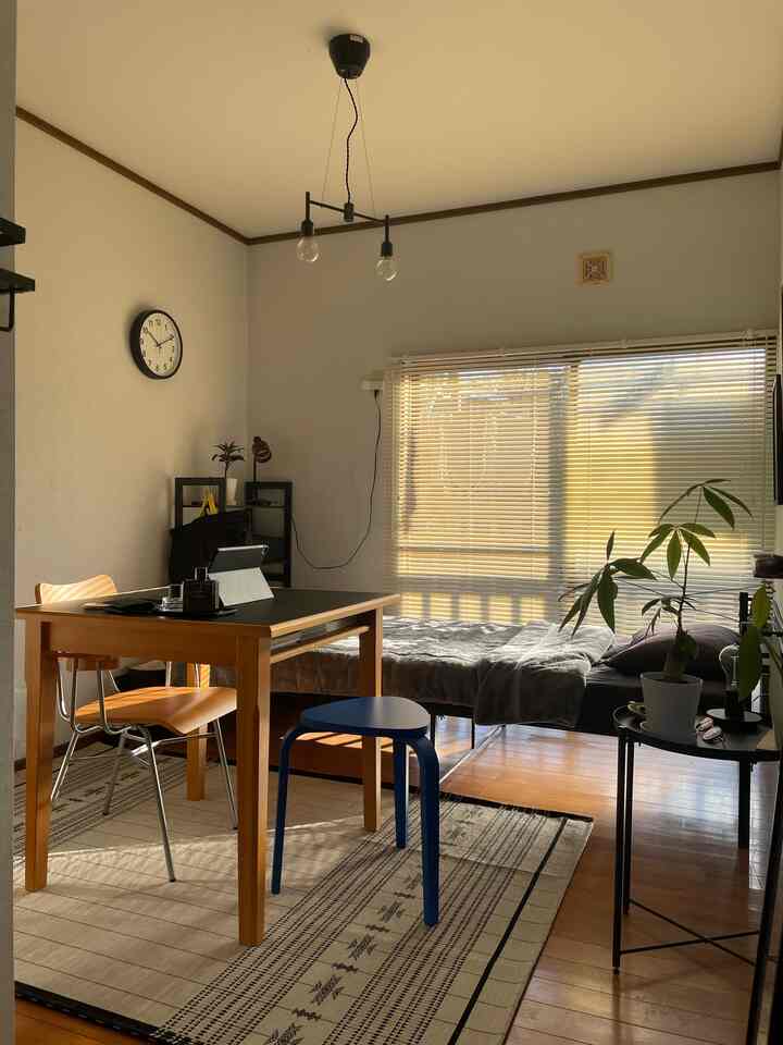 ナチュラルトーンの寝室、ダイニングテーブルと青いスツール、ベッド、植物が配置された雰囲気のある空間