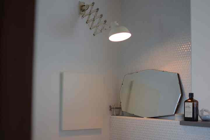 白いタイルと白のシザーランプ、イギリスのアンティークカットガラスの鏡が配置されたモダンなバスルーム空間