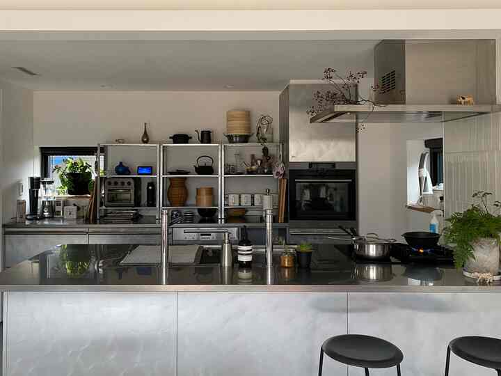 白を基調としたキッチン、ステンレスの棚と調理器具が配置されたモダンな空間