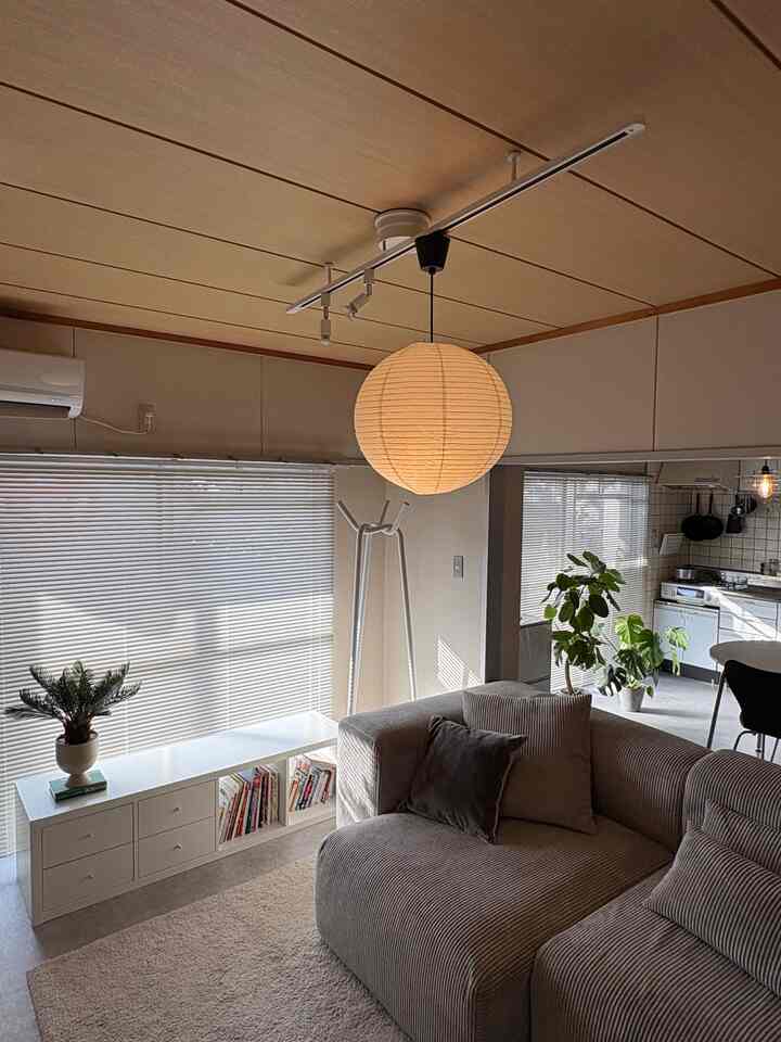 ベージュと白のトーンが調和した6畳のリビングとキッチン、ソファや植物、ペンダントライトが配置された雰囲気のあるインテリア