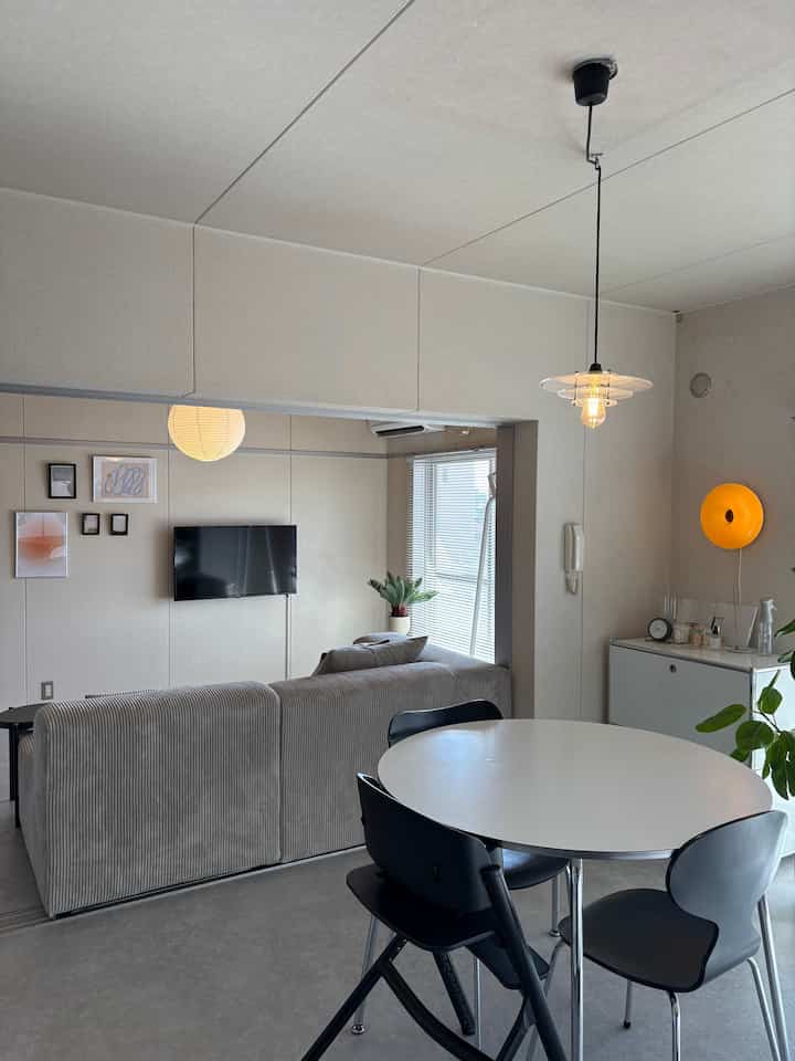 白と黒のトーンの正方形ダイニング、丸テーブルと椅子、グレーのソファが配置されたシンプルでモダンな空間