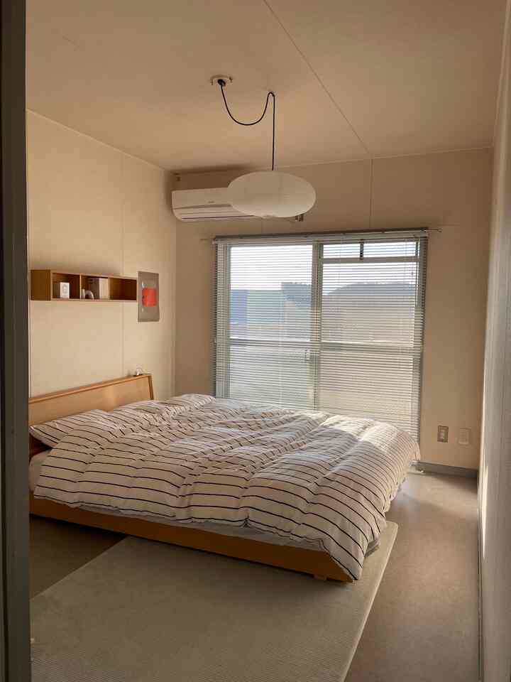 ナチュラルな色調の6畳寝室、木製ベッドとストライプの掛け布団カバーが配置された落ち着いた空間