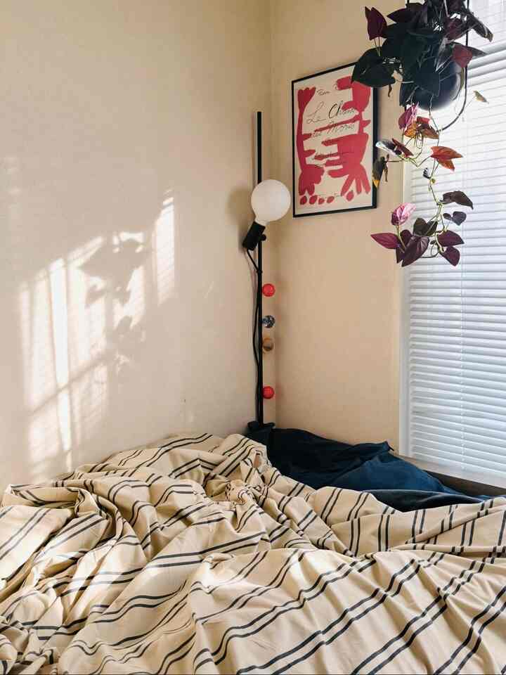 ベージュの壁とネイビーのアクセントがある寝室、ベッドとフロアランプ、垂れ下がる植物が自然な雰囲気を演出