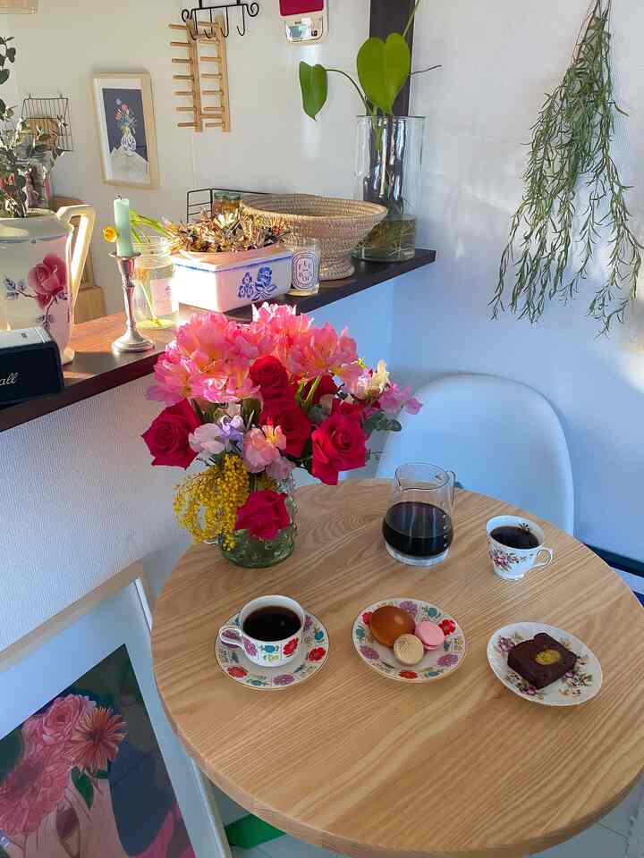 ナチュラルな木目調のラウンドテーブルにホームカフェセットと鮮やかな花が置かれたカフェ風ダイニング