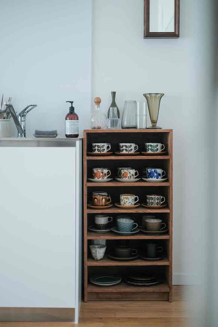 ホワイトと木目調の調和が取れたキッチン、木製の棚に多様なティーカップとコースターが美しく並べられた雰囲気のあるインテリア