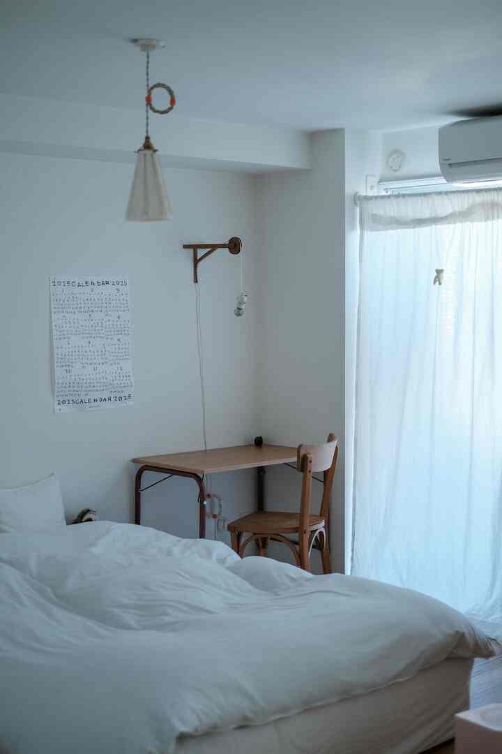 白と茶色の色調の寝室、小さなデスクと椅子が配置されたシンプルで落ち着いた雰囲気のインテリア