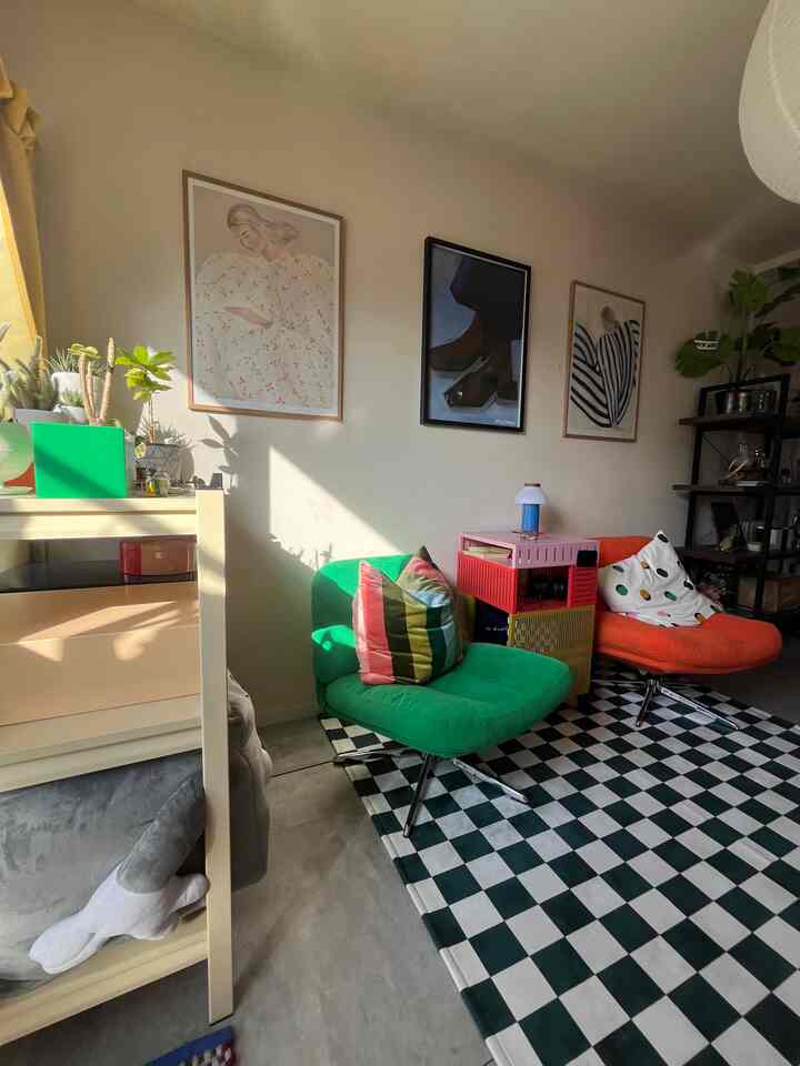 明るい自然光が差し込む白い壁のリビング、緑とオレンジのアームチェアとチェッカーボード柄のラグが配置された雰囲気のある空間