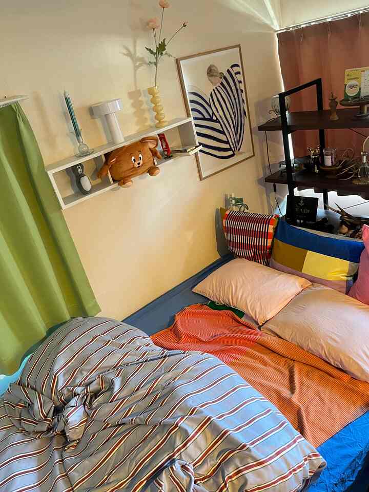 白い壁と緑のカーテンがあるナチュラルな寝室、カラフルなクッションと居心地の良い寝具が配された雰囲気のあるインテリア